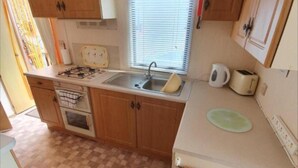 A compact kitchen with wooden cabinets, a gas stove, a sink, and a window with blinds.
