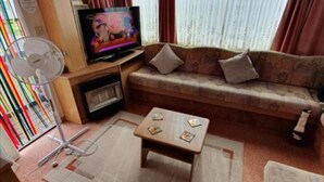 A compact living space with a sofa, a small coffee table, a television, and a fan.
