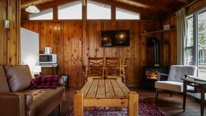 A cozy cabin interior with a wooden interior, a television mounted on the wall, a fireplace, a sofa, and a dining table. - Rustic Muskoka Cabin on the Lake- Port Severn (Port Severn Road)