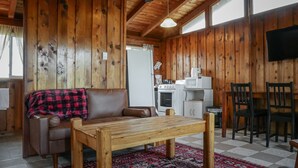 A wooden cabin interior with a sofa, a wooden table, a kitchen area with a stove and microwave, and a TV mounted on the wall. - Rustic Muskoka Cabin on the Lake- Port Severn (Port Severn Road)