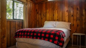 A wooden cabin bedroom with a bed, a window with curtains, and a small table. - Rustic Muskoka Cabin on the Lake- Port Severn (Port Severn Road)