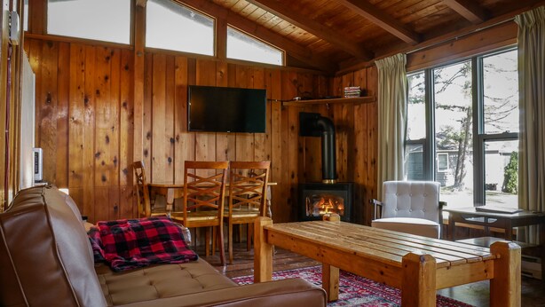 A cozy cabin interior with a wooden interior, a fireplace, a television, and a view of the outside. - Rustic Muskoka Cabin on the Lake- Port Severn (Port Severn Road)