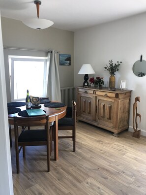 Un comedor con una mesa y sillas de madera, un aparador con adornos y vistas al exterior a través de una ventana con cortinas.