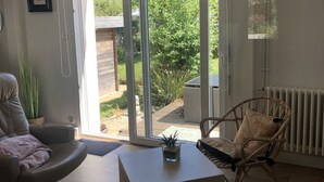Una sala moderna con un sofá de cuero, una silla de mimbre, una mesa de centro de vidrio y vista a un jardín a través de grandes puertas correderas de cristal.