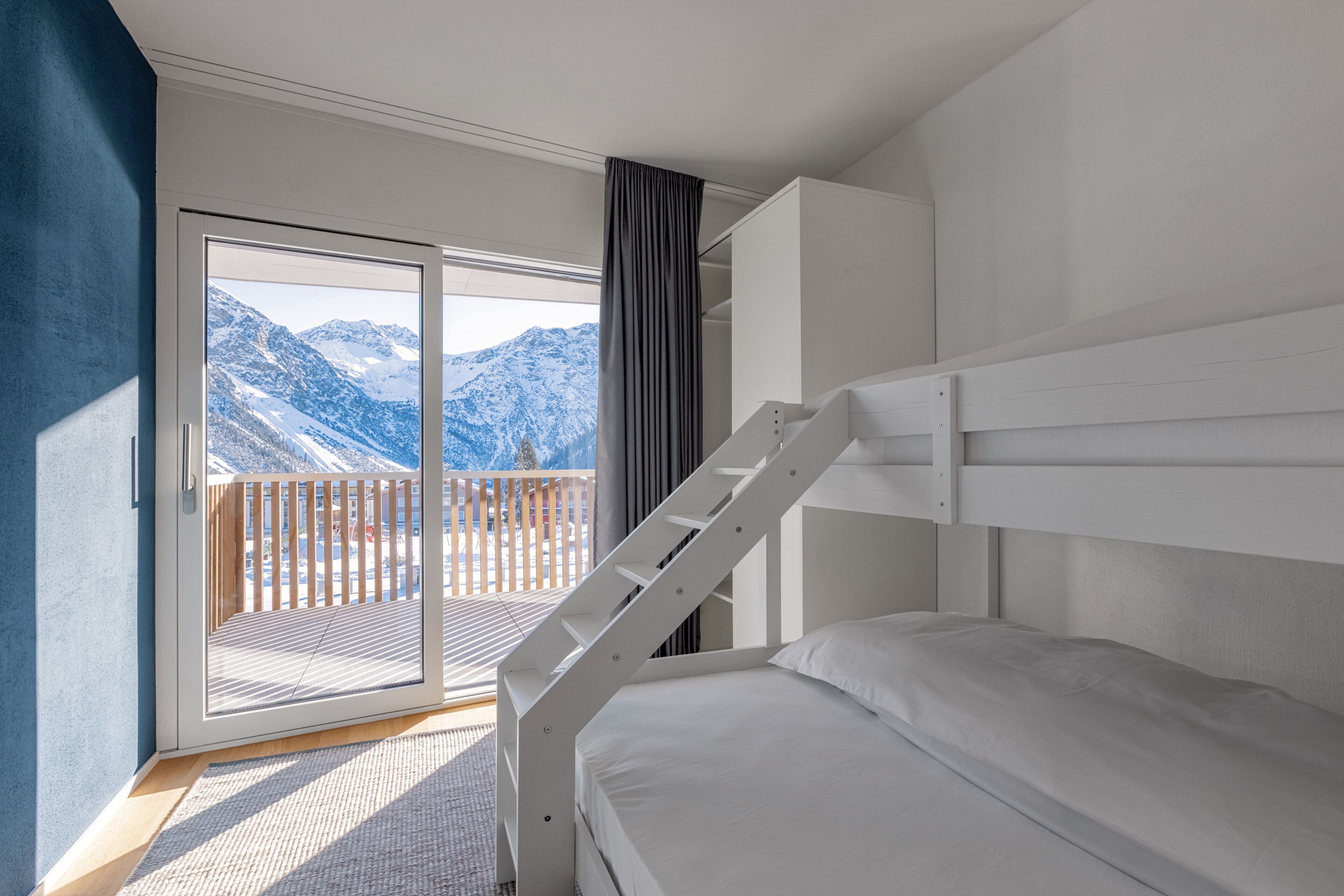 A bedroom with a bunk bed, a sliding glass door leading to a balcony with a mountain view.