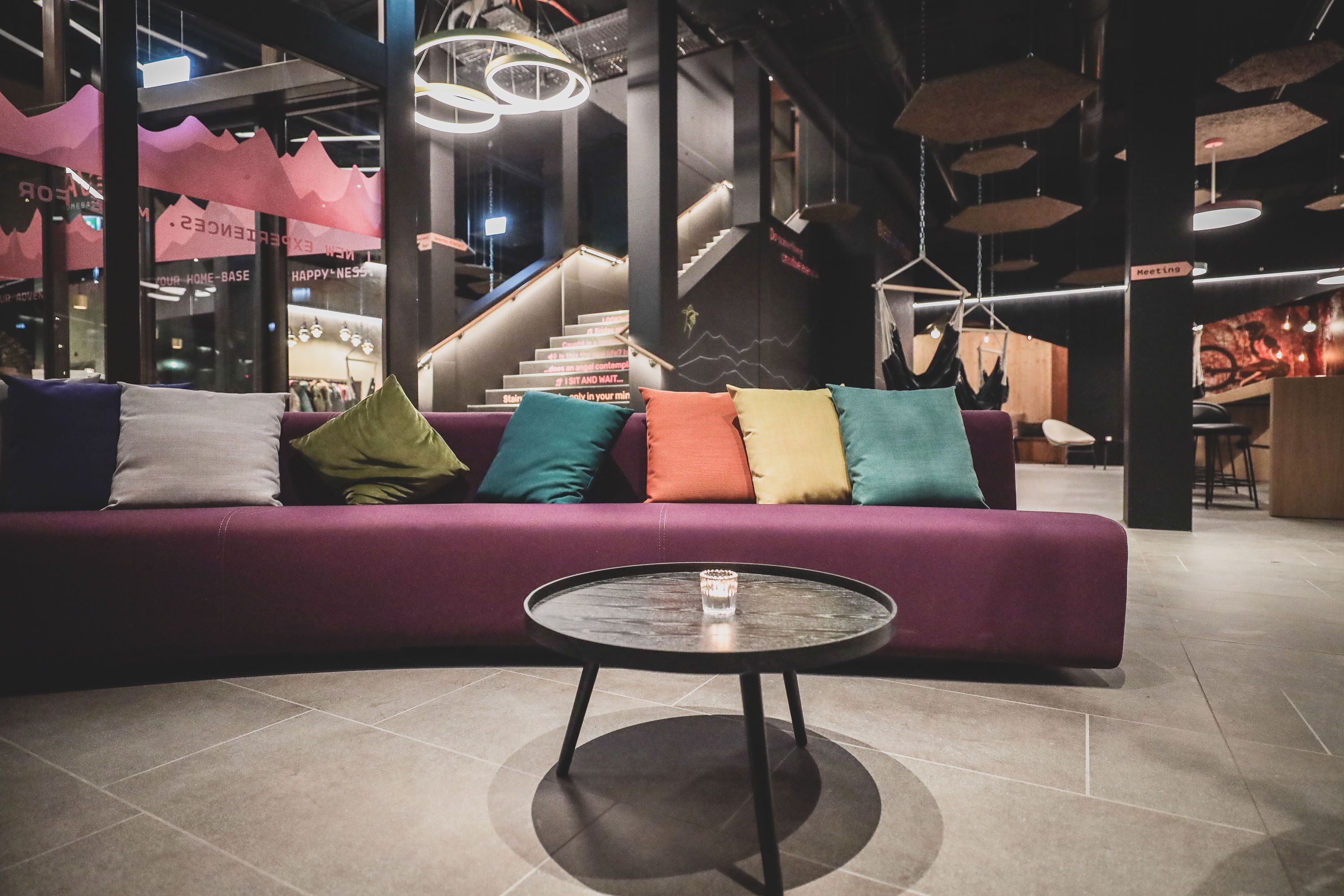 A modern interior with a purple sofa, a glass-top coffee table, and a staircase in the background.