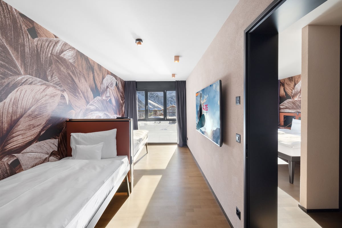 Una habitación de hotel moderna con una cama grande, un televisor montado en la pared y vistas a la montaña a través de la ventana.