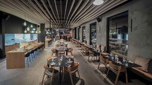 Um restaurante moderno com um balcão extenso, várias mesas de jantar e um espaço de bar.