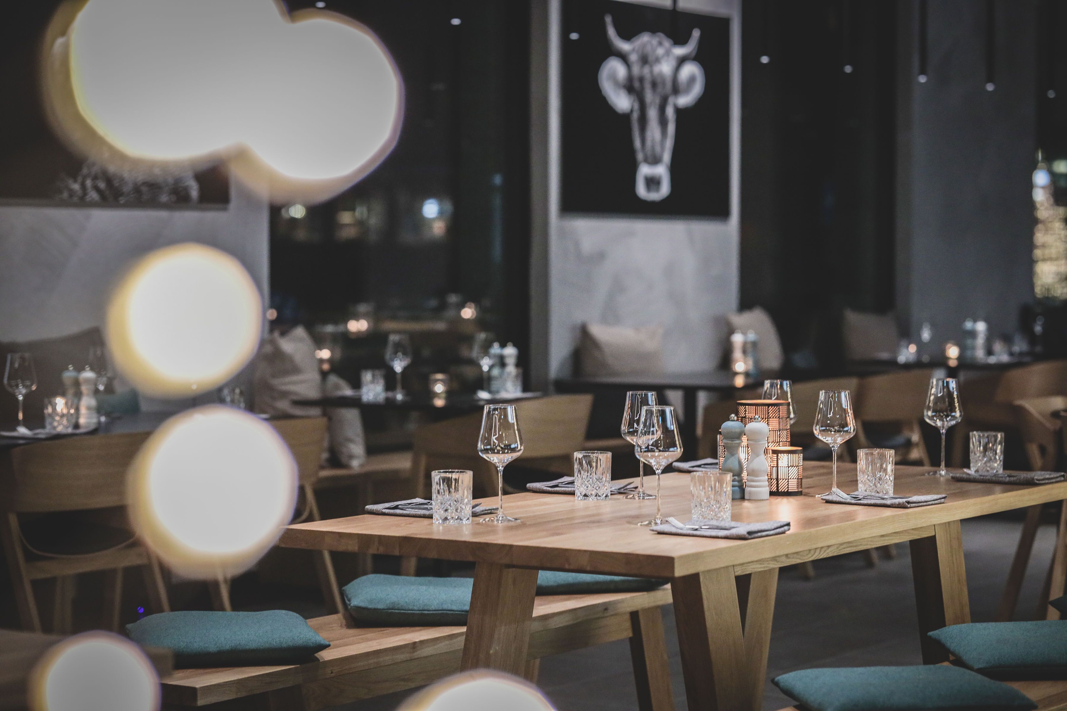 A restaurant with wooden tables and chairs, each set with wine glasses and cutlery.