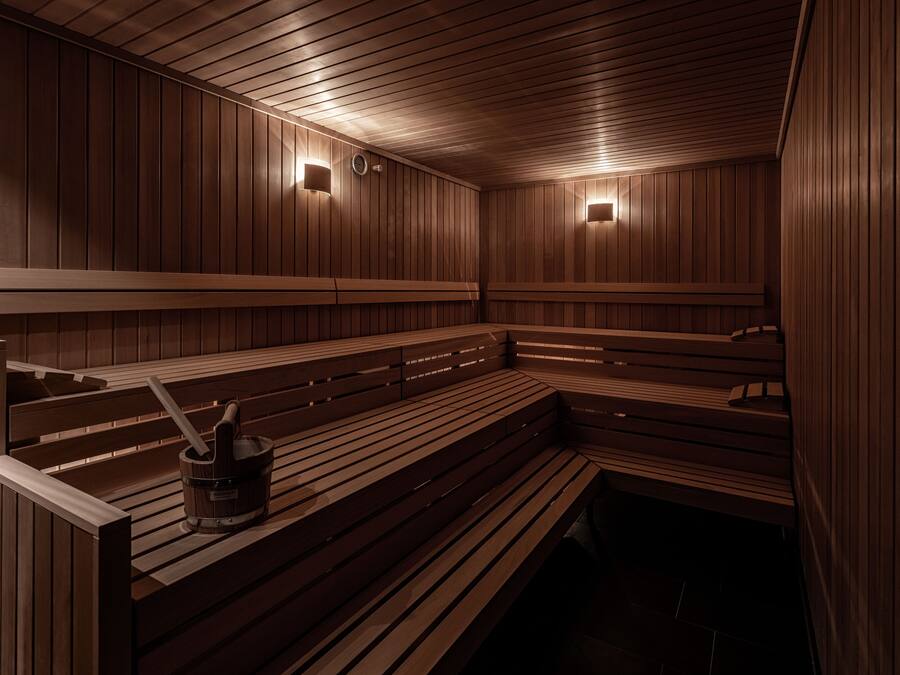 A sauna with wooden benches and walls, two wall-mounted lights, and a bucket with a brush.