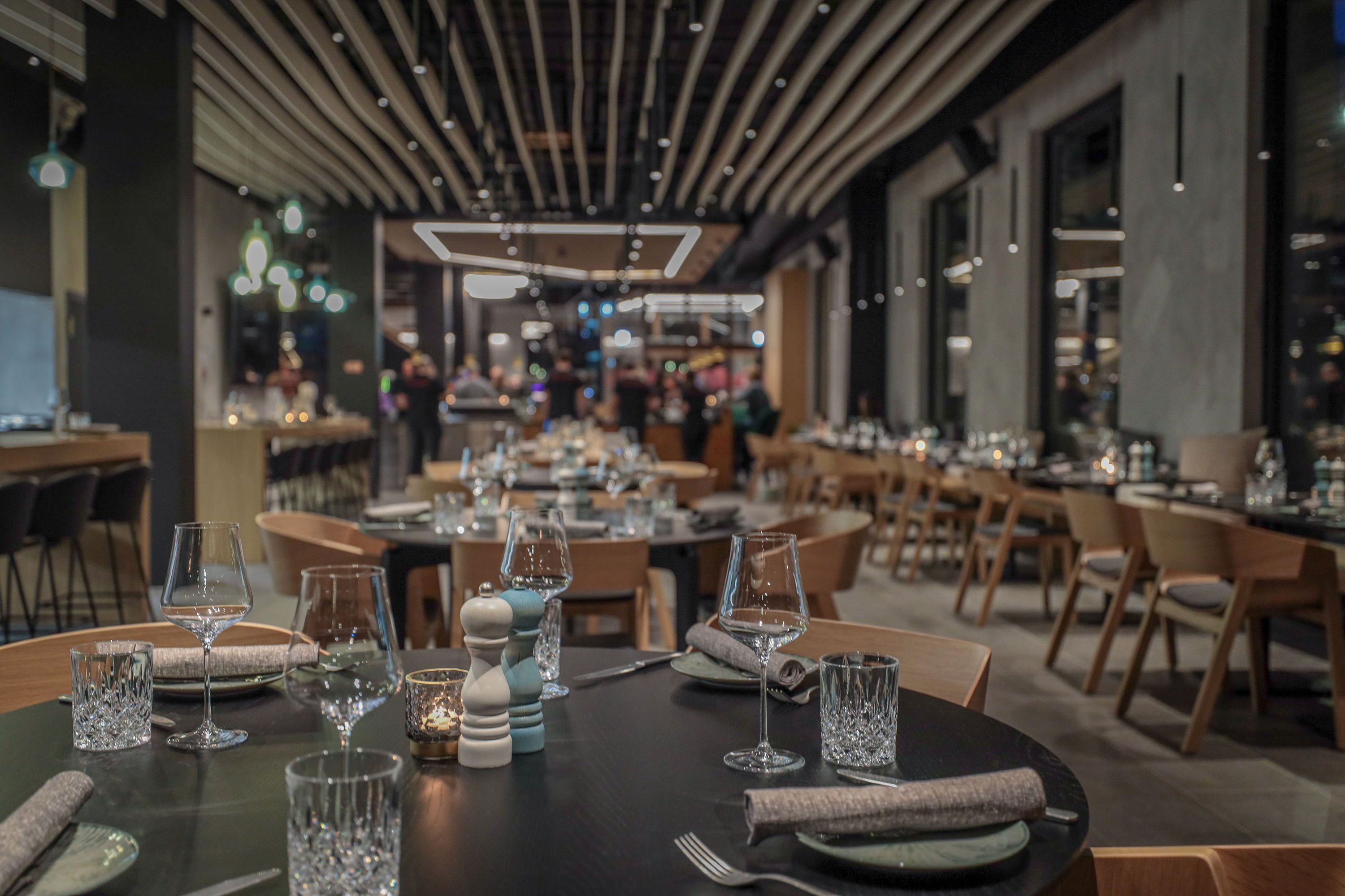 A restaurant with tables set for dining, featuring modern decor and ambient lighting.