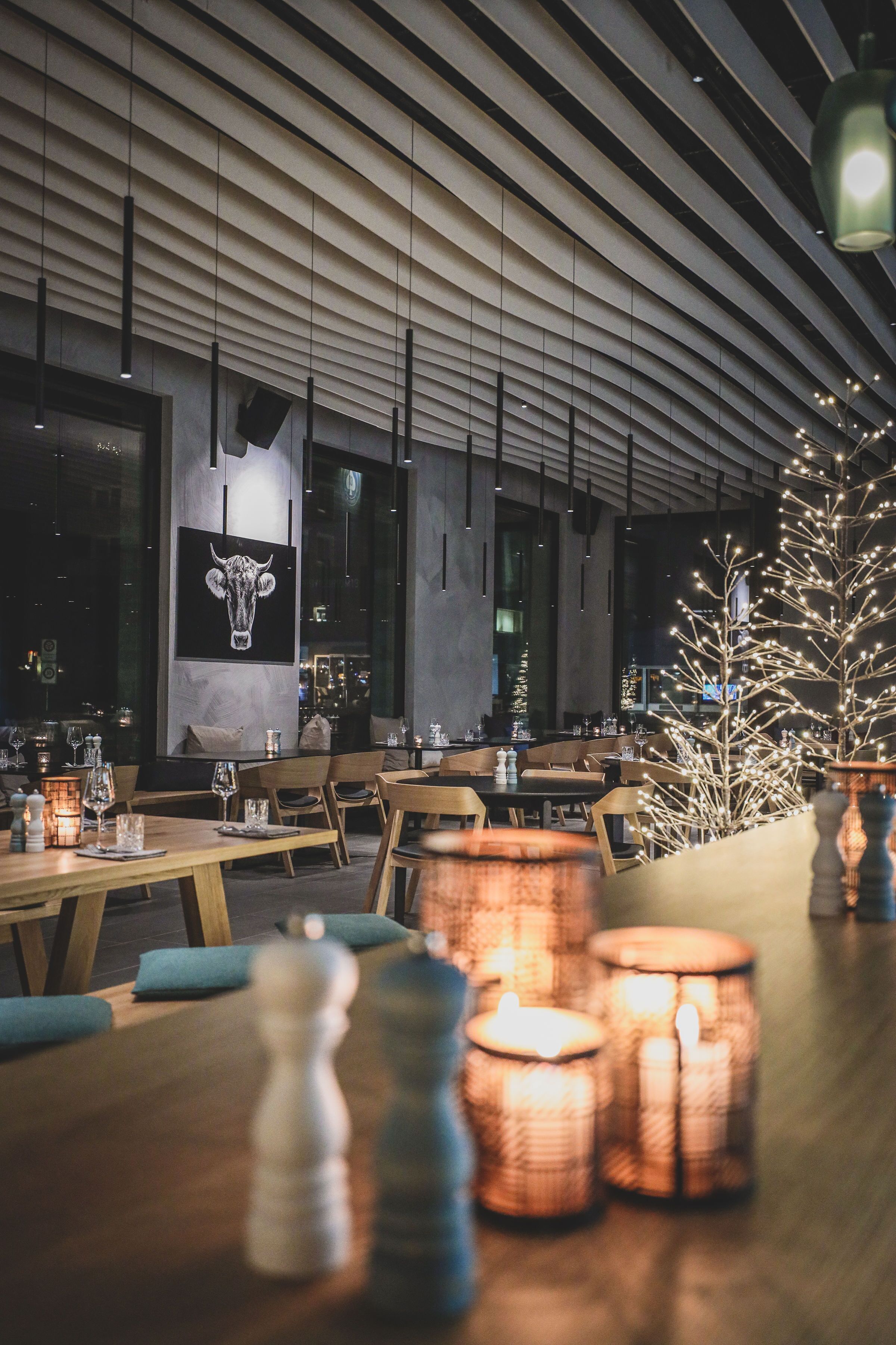 Un intérieur de restaurant moderne avec des tables en bois, des tables éclairées à la bougie et un arbre décoratif.