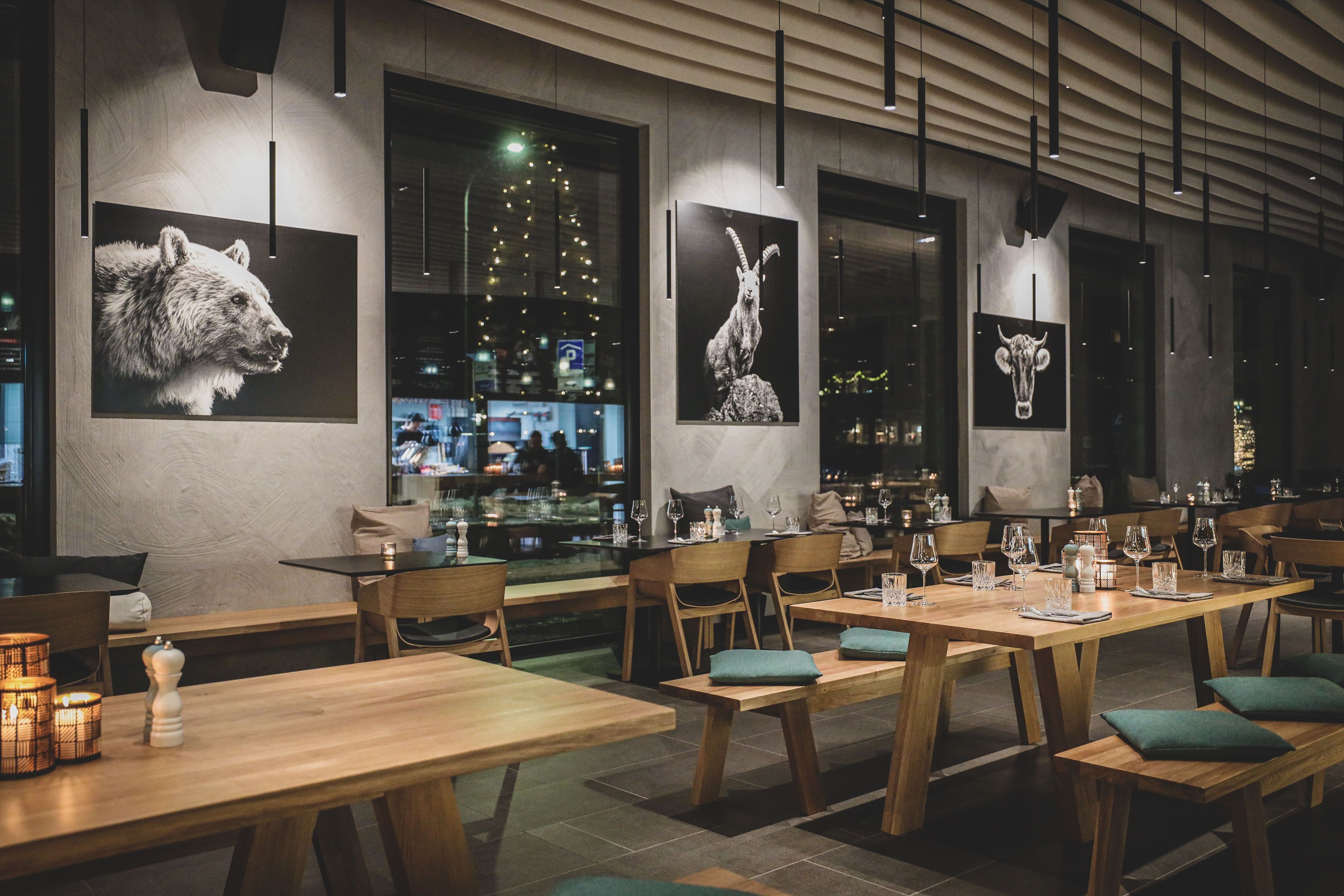 Een restaurant met houten tafels en stoelen, grote ramen en kunstwerken aan de muur.