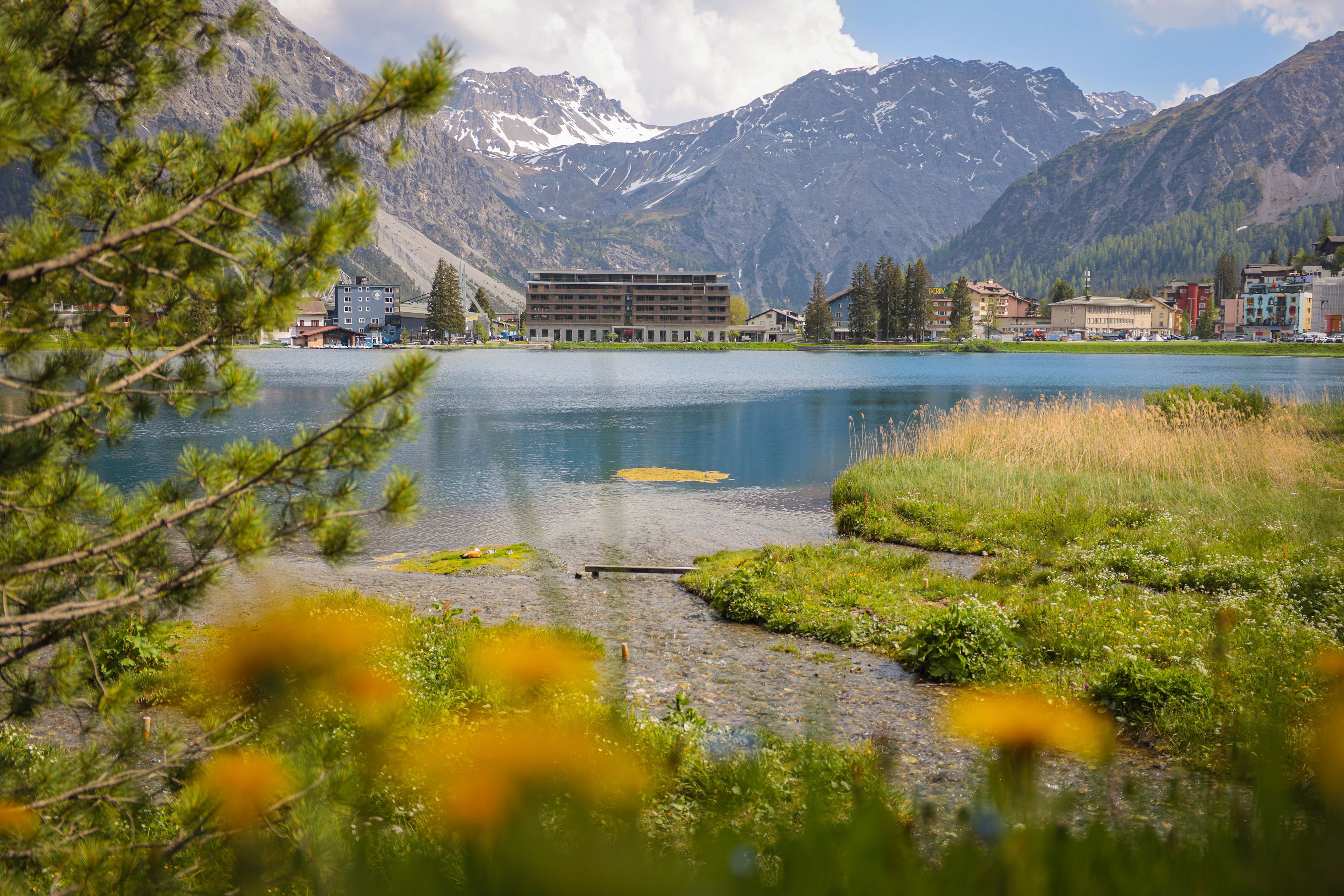 A hotel with multiple floors, a lake in the foreground, and mountains in the background.