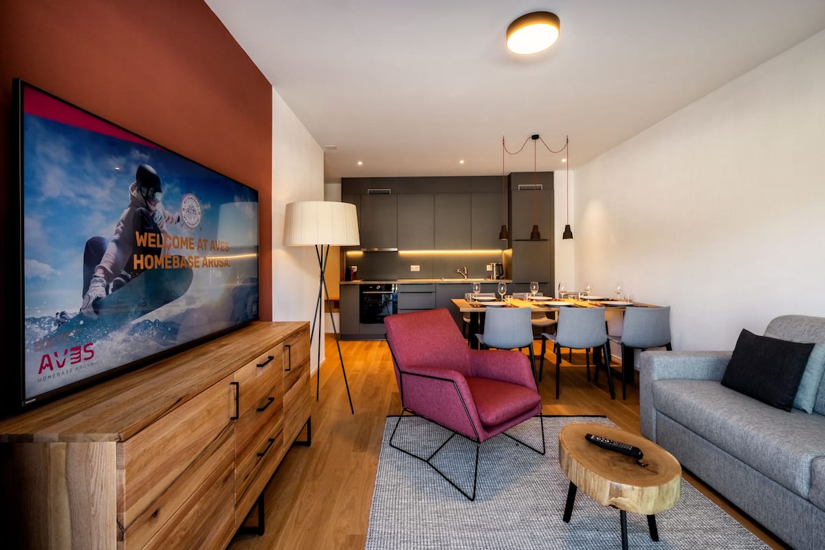 Una sala de estar moderna con una televisión de pantalla plana, un sillón rojo, un sofá gris y una mesa de centro de madera.