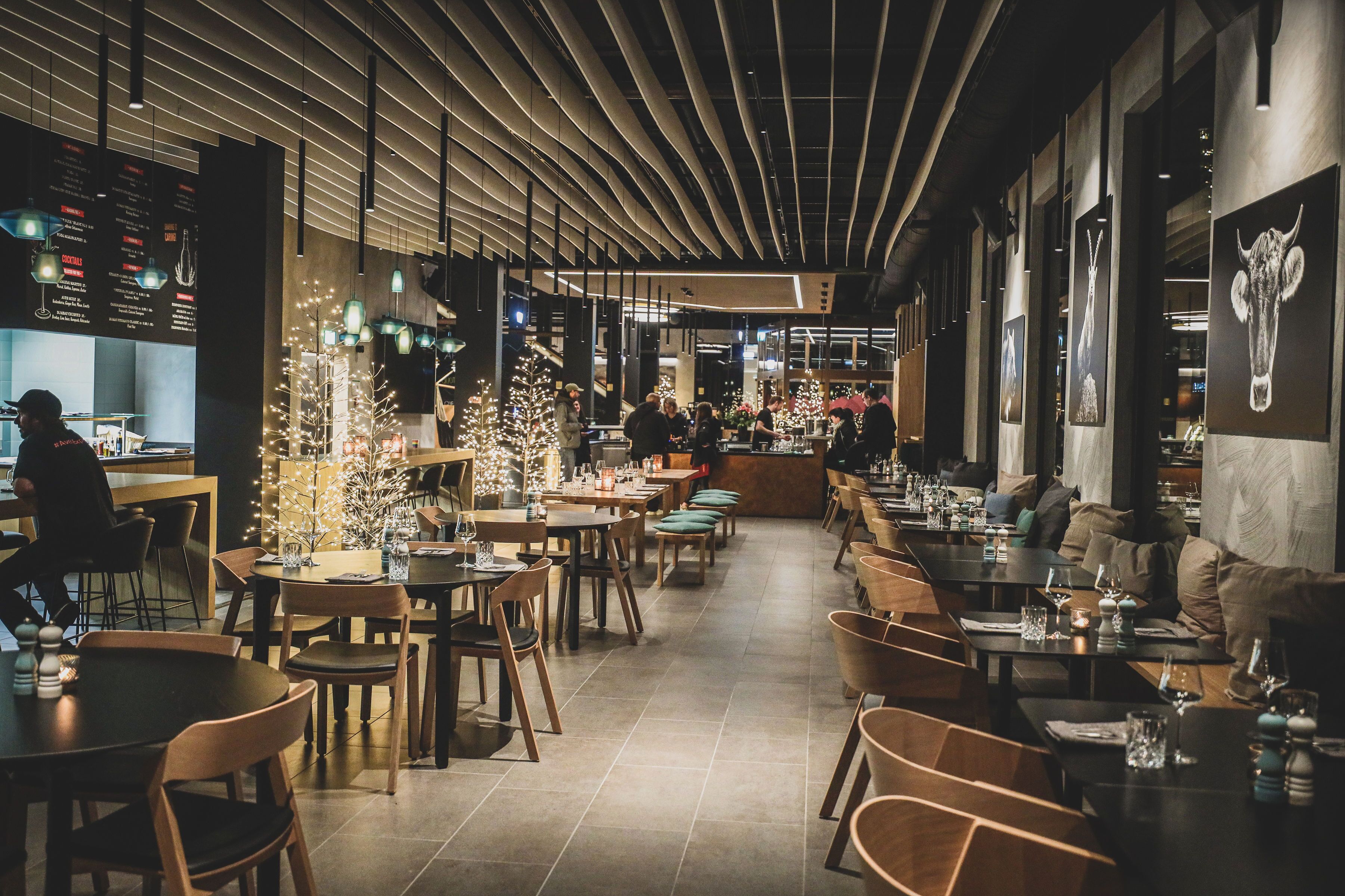A modern restaurant interior with wooden tables and chairs, a bar area, and a Christmas tree decoration.