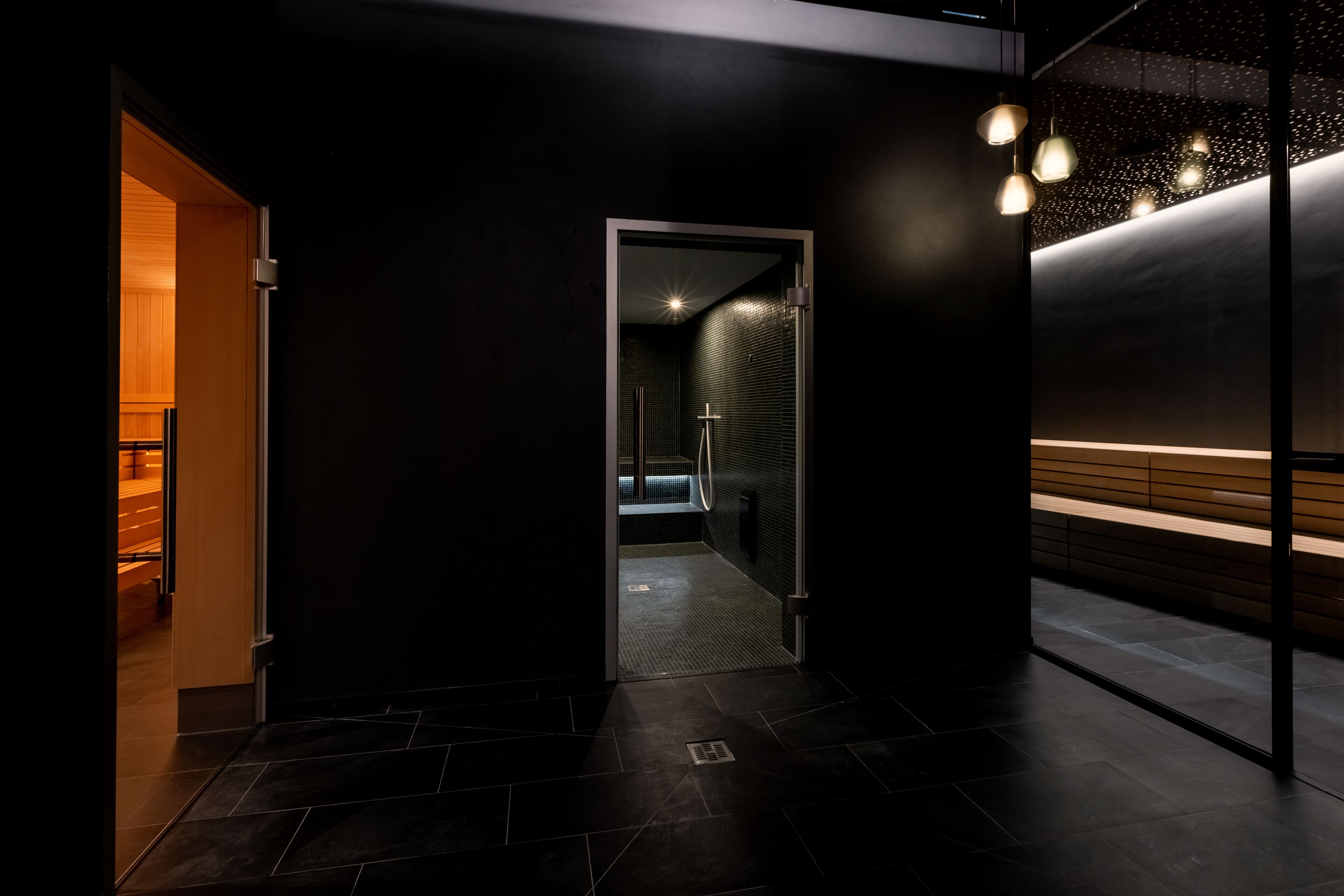 A modern hallway with a dark floor, a glass door leading to a bathroom, and a bench with a light-colored backrest.
