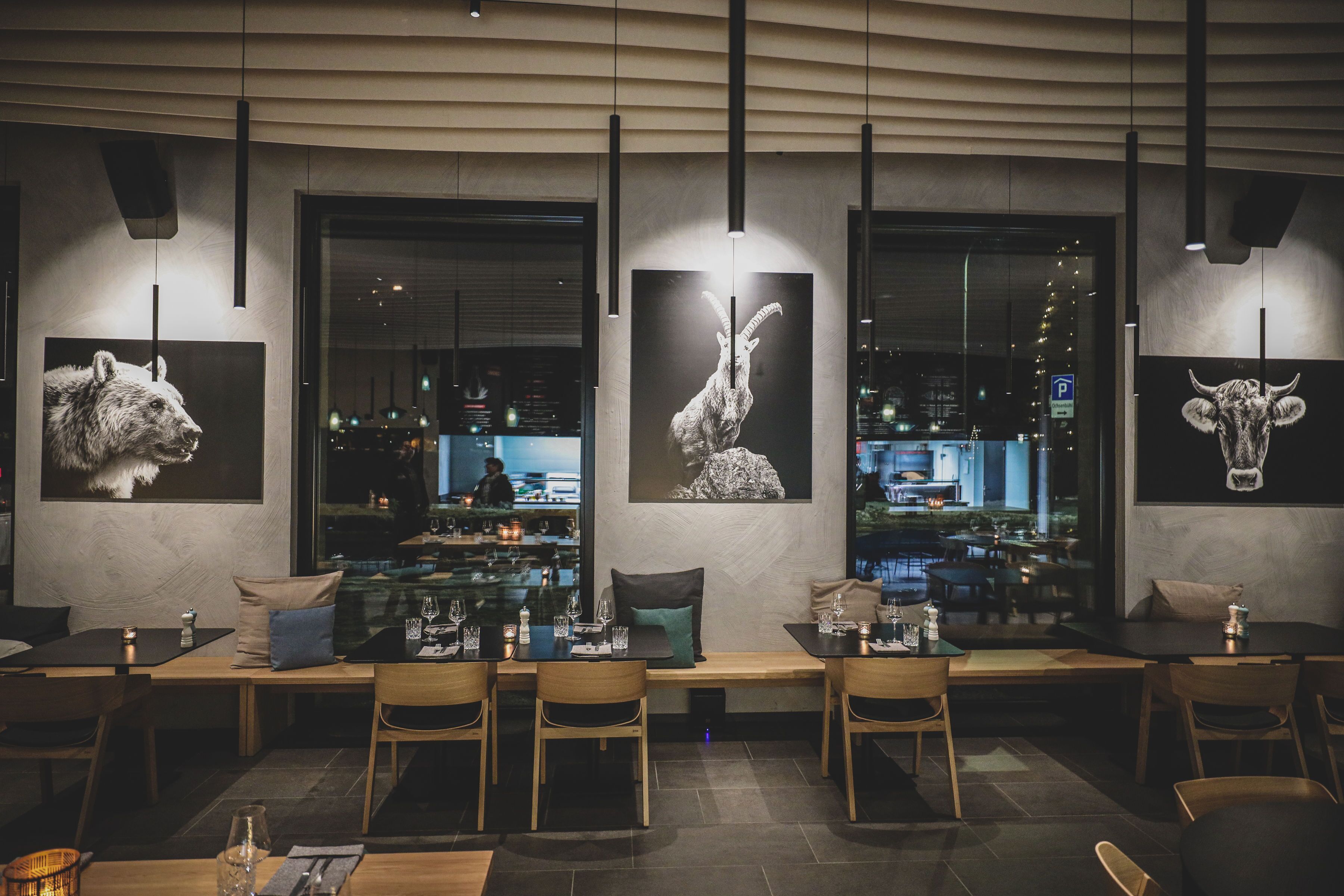 A modern restaurant interior with wooden furniture, large windows, and city views.