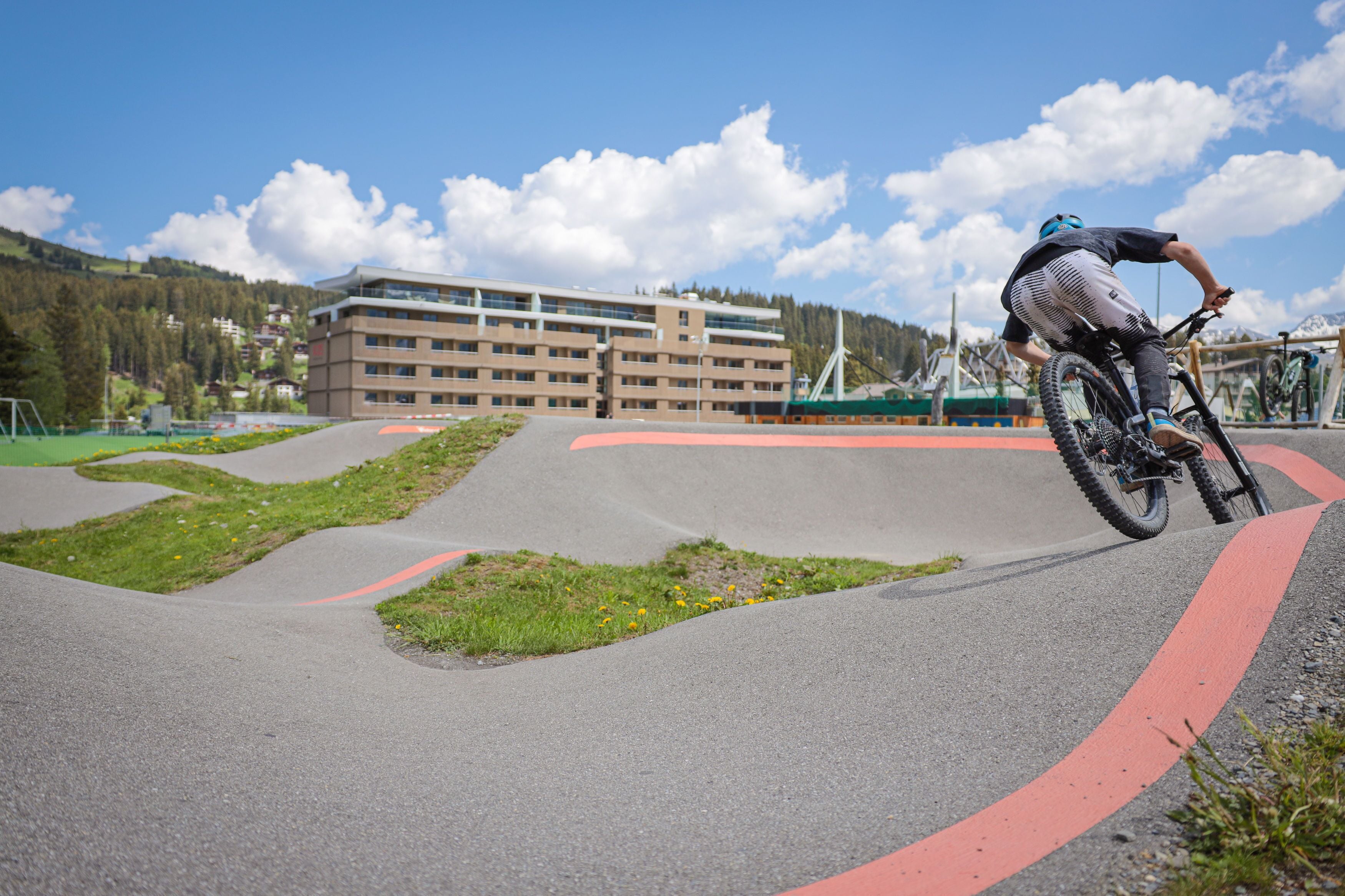 A person riding a bicycle on a curved track with a building in the background.