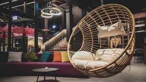 Um interior moderno com uma cadeira de balanço de vime, um sofá roxo com almofadas coloridas e uma escada com uma placa.