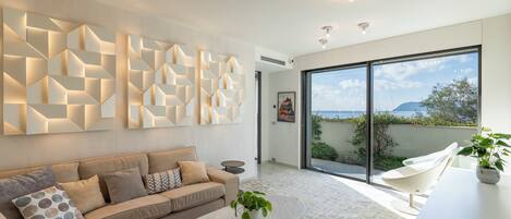 Un salon moderne avec un canapé beige, une table basse en marbre et une œuvre d’art murale aux motifs géométriques.