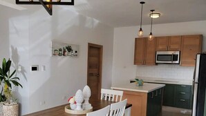 A modern kitchen with wooden cabinets, a central island, and a dining area with white chairs. - Luxury Apt w/ Pool 5-min Walk to Beach & Ocean World (Cofresi)