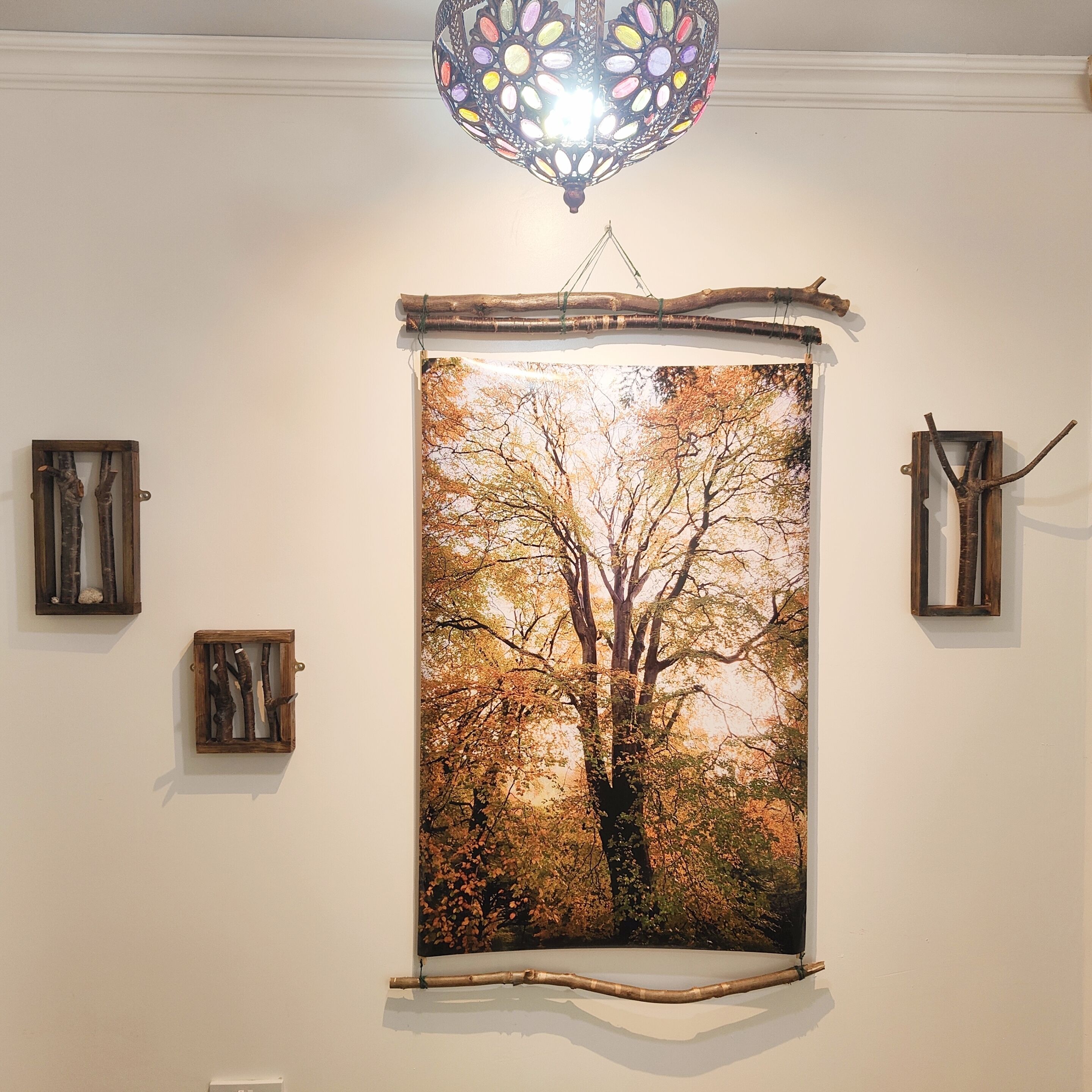 A framed photograph of a tree with autumn leaves on a wall, a hanging light fixture, and two small wooden frames.
