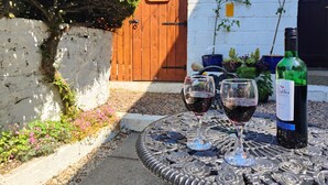 A table with two wine glasses and a bottle of wine, a wooden door, and a white wall with a plant. - Mourne Mountain Art Apartments (Newcastle)