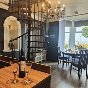 A modern interior with a wooden bar area, a spiral staircase, and a dining area with a view of the sea. - Mourne Mountain Art Apartments (Newcastle)