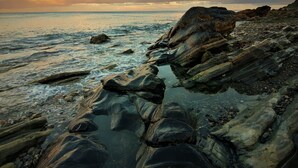 A rocky shoreline with clear water and a sunset in the background. - Mourne Mountain Art Apartments (Newcastle)
