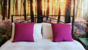 A bed with a forest-themed wall mural, two pillows, and a nightstand. - Mourne Mountain Art Apartments (Newcastle)