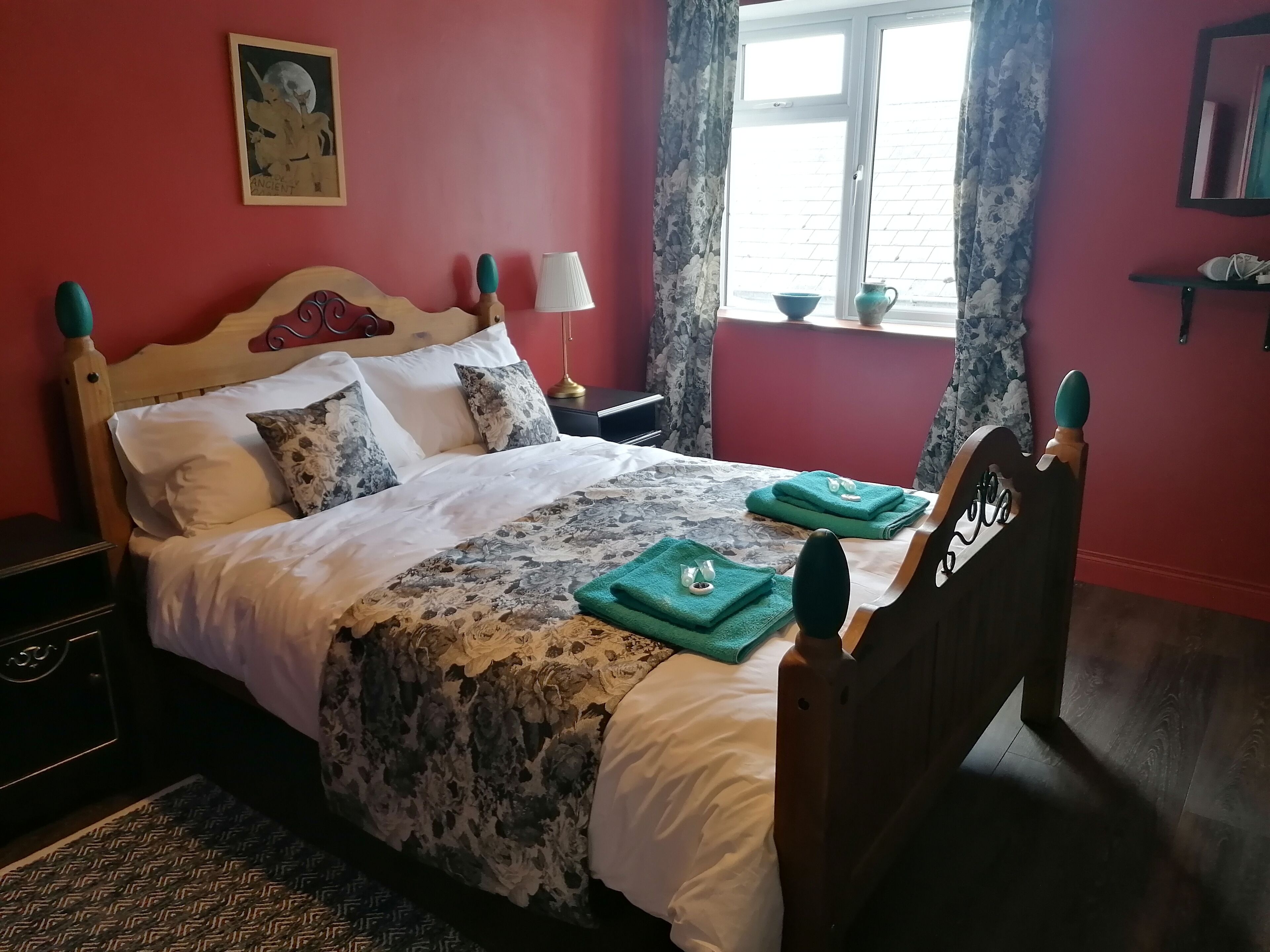 A neatly made bed with floral bedding, a bedside lamp, and a window with curtains.
