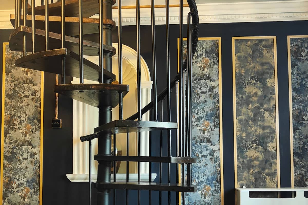 A spiral staircase in a room with dark walls and a large window. The room has a modern design with a mix of dark and light colors.
