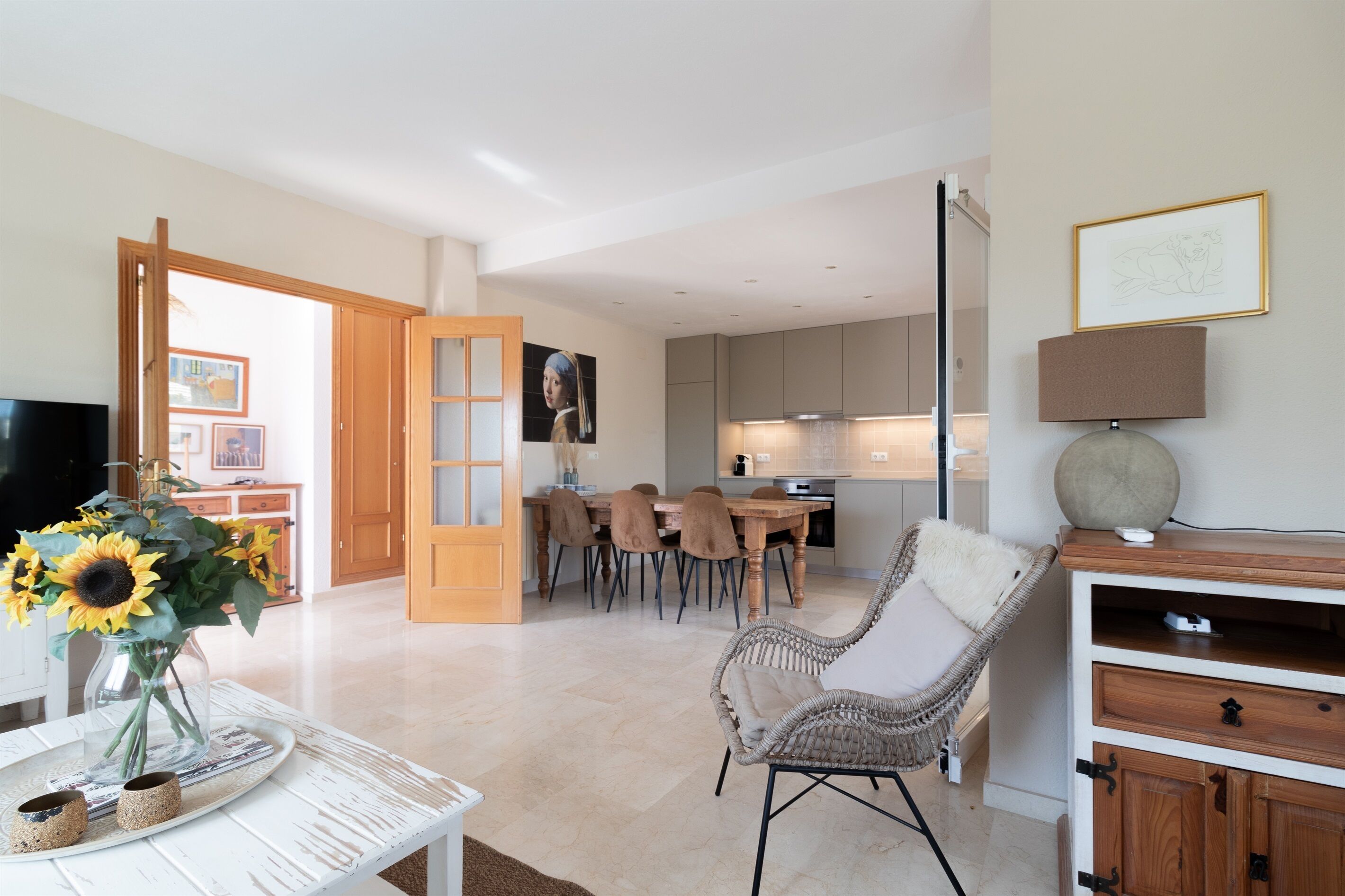 A modern living room with a dining area, a TV, a wicker chair, and a lamp.