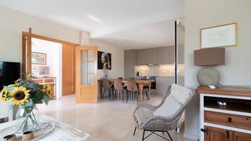 A modern living room with a dining area, a TV, a wicker chair, and a lamp.