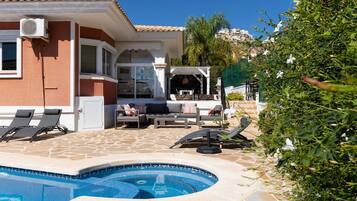 A pool area with lounge chairs, a covered seating area, and a stone-tiled patio.