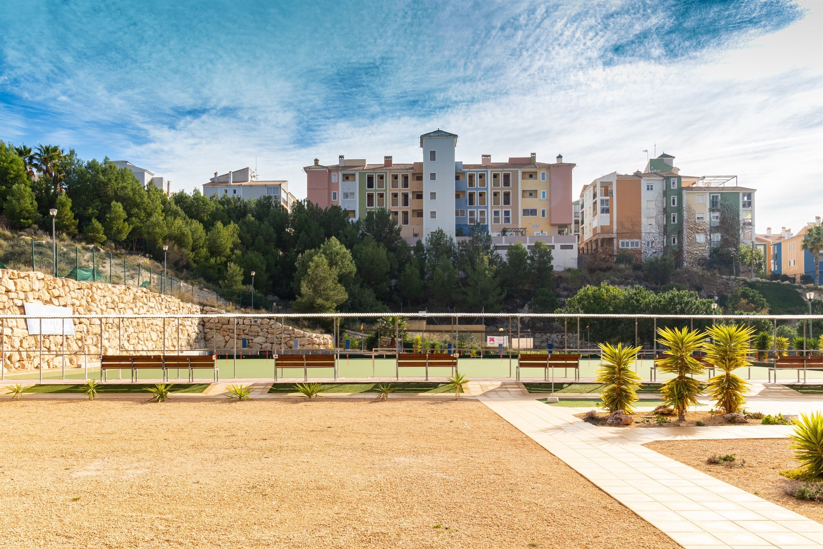 A residential area with multi-story buildings, a paved walkway, and a fenced sports court.