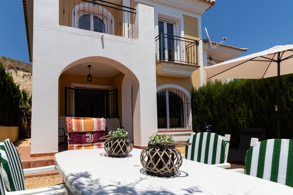 A two-story building with a balcony, outdoor seating area, and potted plants.