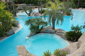 Une grande piscine extérieure divisée en plusieurs zones, entourée de rochers et de palmiers.