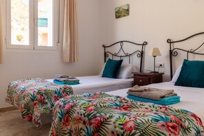 A room with two single beds, a nightstand with a lamp, and a window with curtains.