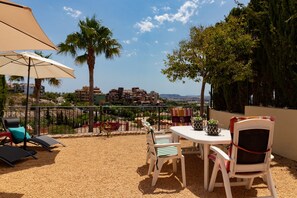 A terrace with outdoor seating, a table, and a view of buildings in the distance.