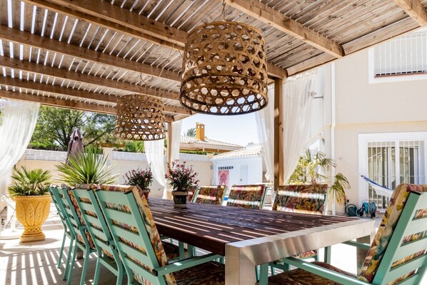An outdoor patio with a wooden pergola, a table with chairs, and potted plants. - Casa Verde 4P guesthouse with private heated pool (Mutxamel, Bonalba)