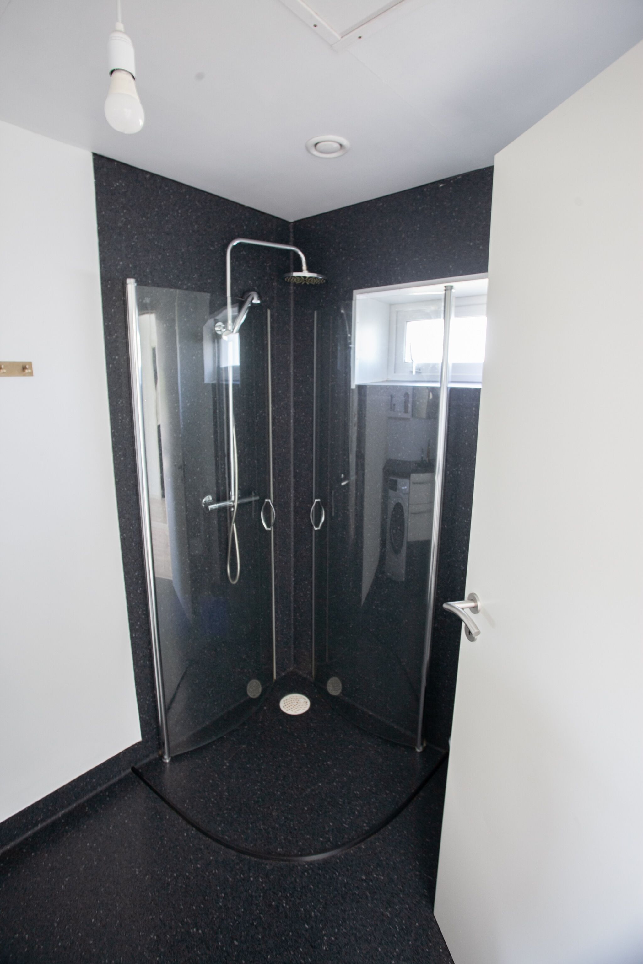 Un baño moderno con ducha envuelta en vidrio, techo blanco y piso oscuro moteado.