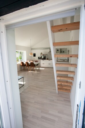 Una cocina moderna con armarios blancos, un comedor con mesa y sillas, y una escalera con escalones de madera.