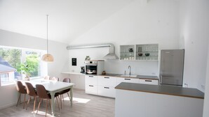 Una cuina moderna amb armaris blancs, una illa gran i una zona de menjador amb taula i caires.