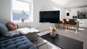 Un saló modern amb un sofà, una taula de centre i un televisió de pantalla plana. Hi ha una zona de menjador amb cadires i una taula, i una cuina amb forn i un rentaplat.