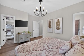 Quarto com cama, guarda-roupa, televisão e duas obras de arte com folhas emolduradas.