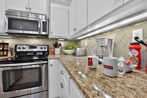 Cozinha moderna com eletrodomésticos de aço inoxidável, bancada de granito e cafeteira.