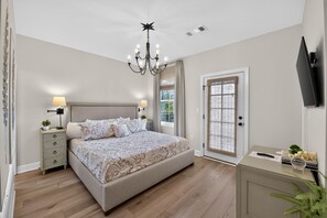 A bedroom with a bed, bedside tables, a chandelier, a television, and a door with a view. - Bama Getaway - Walk to Downtown & Campus!  Luxurious and cozy furnishings! (Tuscaloosa)