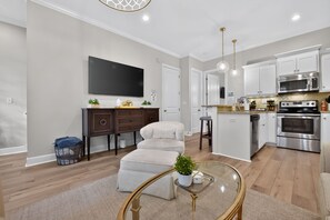 A modern kitchen with stainless steel appliances, a dining area with a sofa, and a flat-screen TV mounted on the wall. - Bama Getaway - Walk to Downtown & Campus!  Luxurious and cozy furnishings! (Tuscaloosa)
